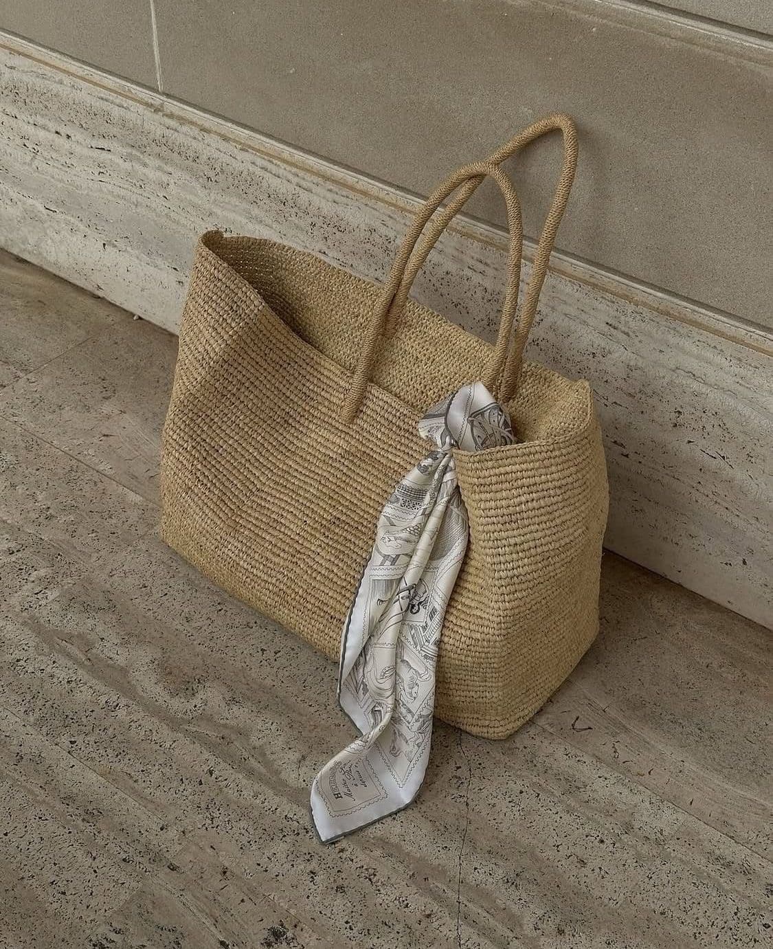A woven bag styled with a silk scarf against warm stone